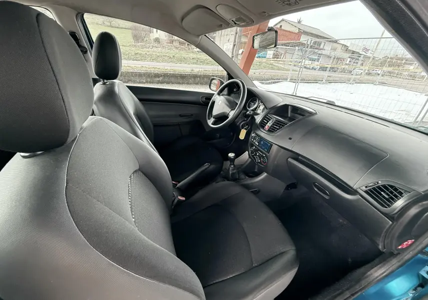 Vue intérieure côté conducteur de la Peugeot 206+ 2011 avec sièges tissu noir et tableau de bord sobre.