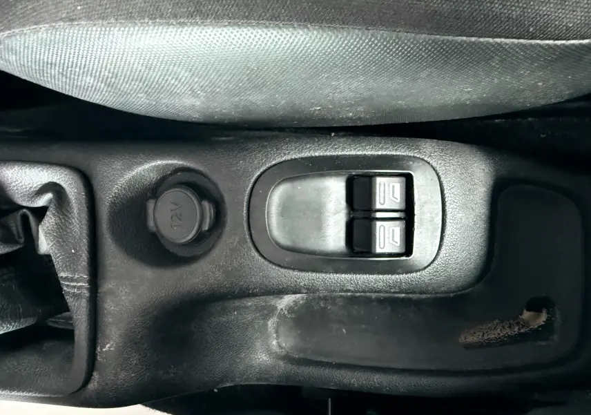 Gros plan sur les commandes de lève-vitres et prise 12V au centre de la console d'une Peugeot 206+ bleue.