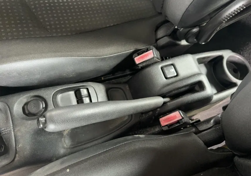 Vue rapprochée de la console centrale noire avec frein à main, boutons de lève-vitres et ceintures de sécurité rouges.