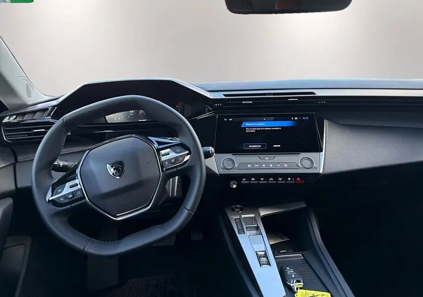 Intérieur de la Peugeot 308 2025, vue du poste de conduite avec volant multifonction et écran tactile central.