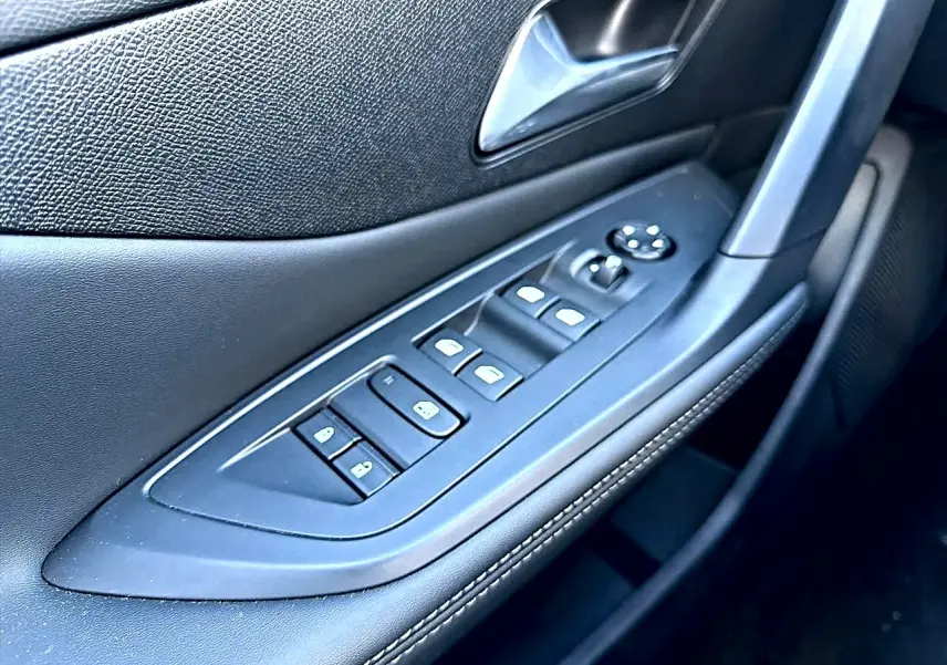 Gros plan sur la commande des vitres électriques et rétroviseurs côté conducteur en cuir noir avec surpiqûres blanches.