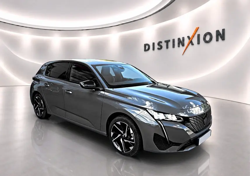 Peugeot 308 gris selenium vue 3/4 avant droit dans un showroom lumineux avec jantes alu noires et logo Distinxion.