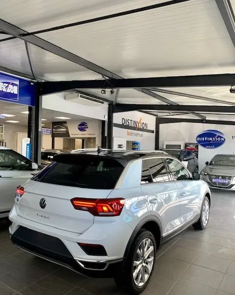 Volkswagen T-Roc blanc en 3/4 arrière droit dans un showroom avec feux arrière LED allumés et toit noir.