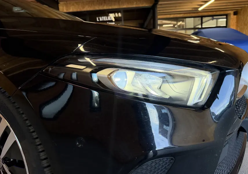 Gros plan sur le phare avant droit noir brillant d'une Mercedes Classe A 2022, avec jante alu partiellement visible.