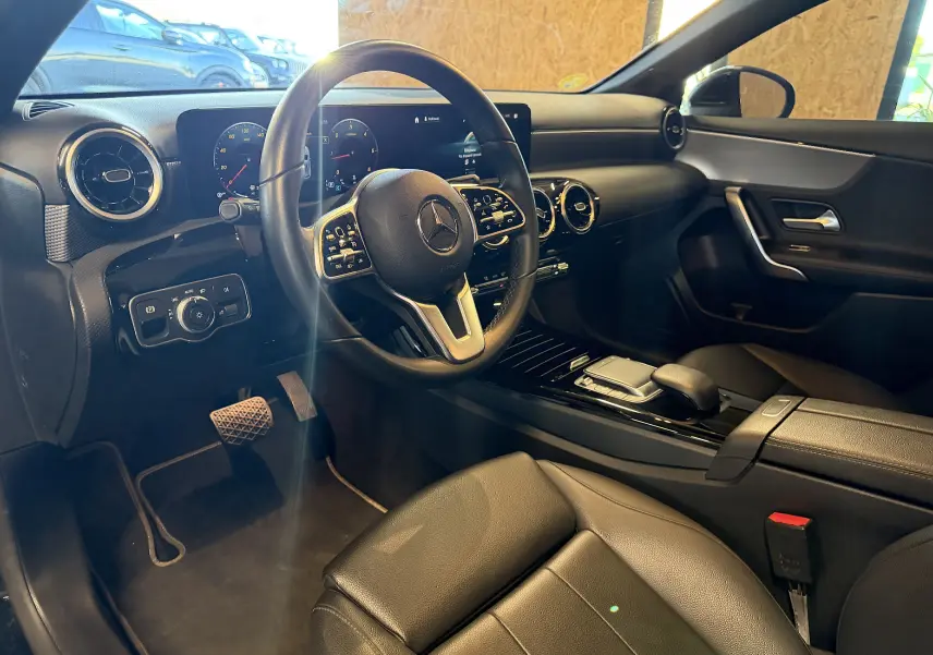 Vue intérieure côté conducteur de la Mercedes Classe A 2022 noire, avec volant cuir multifonctions et écran tactile.