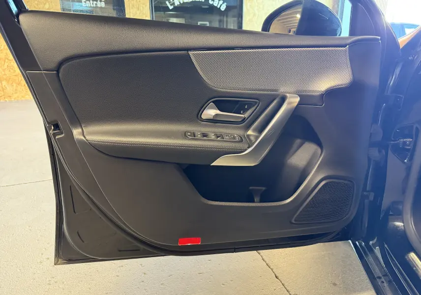 Vue intérieure du panneau de porte avant gauche noir de la Mercedes Classe A 2022 avec commandes électriques et haut-parleur intégré.