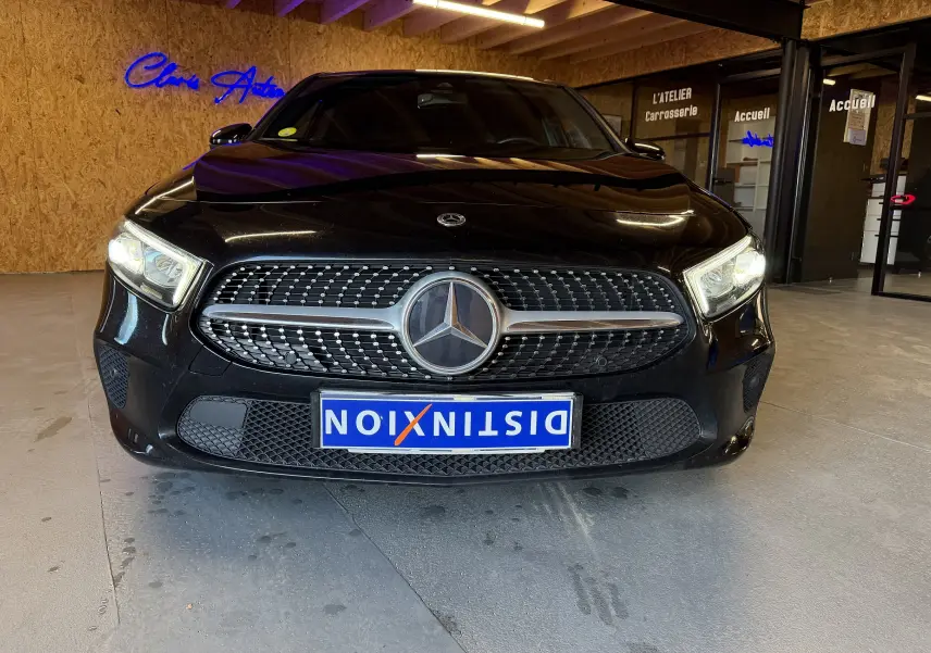 Vue avant d'une Mercedes Classe A noire avec calandre diamantée et phares allumés dans un garage.