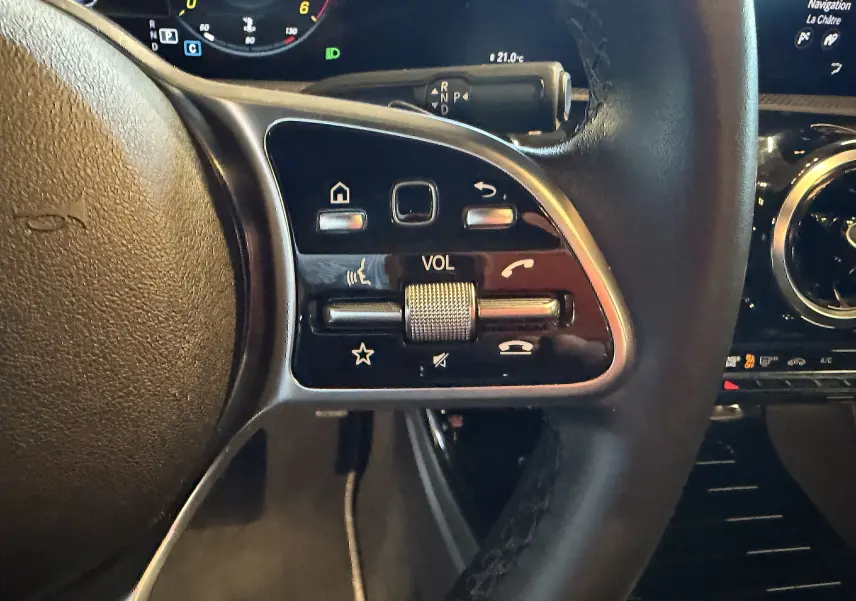 Gros plan sur les commandes multifonctions du volant cuir noir d'une Mercedes Classe A 2022, avec écran tactile en arrière-plan.
