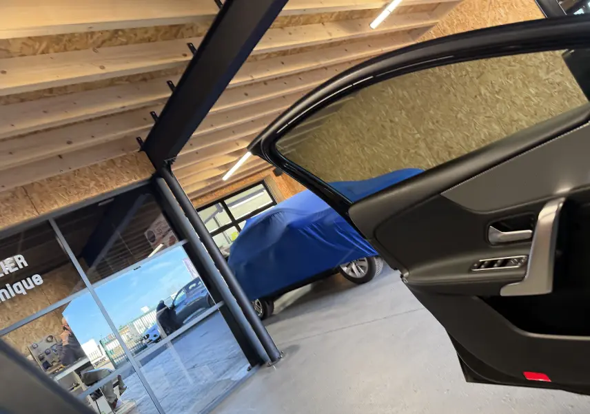 Vue intérieure côté droit de la porte ouverte d'une Mercedes Classe A noire, avec vitrage teinté visible en garage.