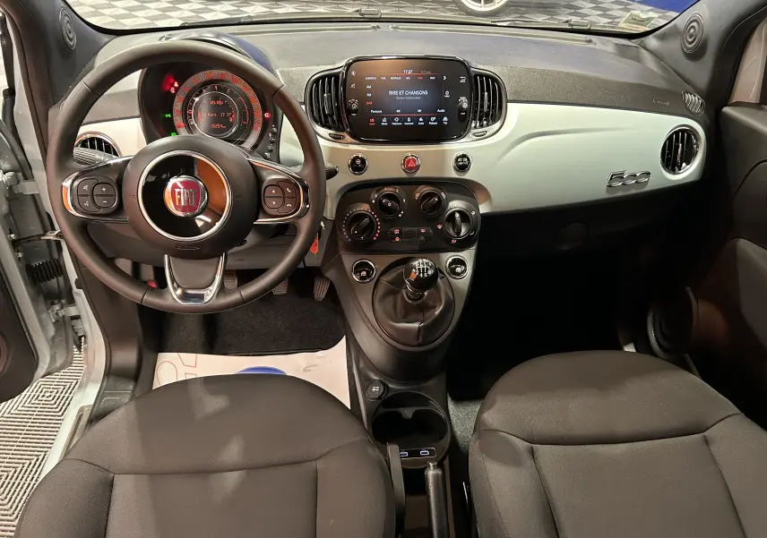 Intérieur de FIAT 500 2023 vue de face, tableau de bord blanc, volant multifonction et écran tactile central allumé.