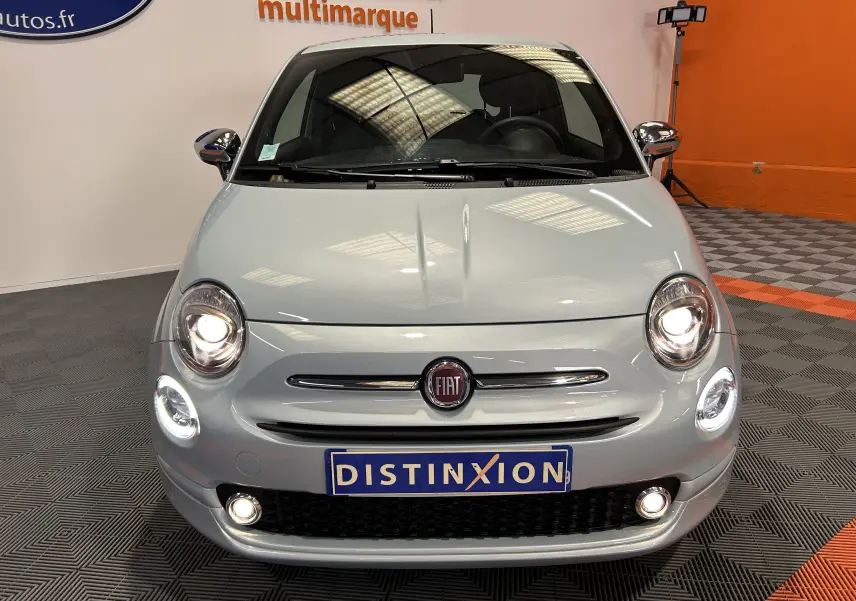 Vue avant d'une FIAT 500 2023 en gris clair avec phares allumés et plaque d'immatriculation Distinxion visible.