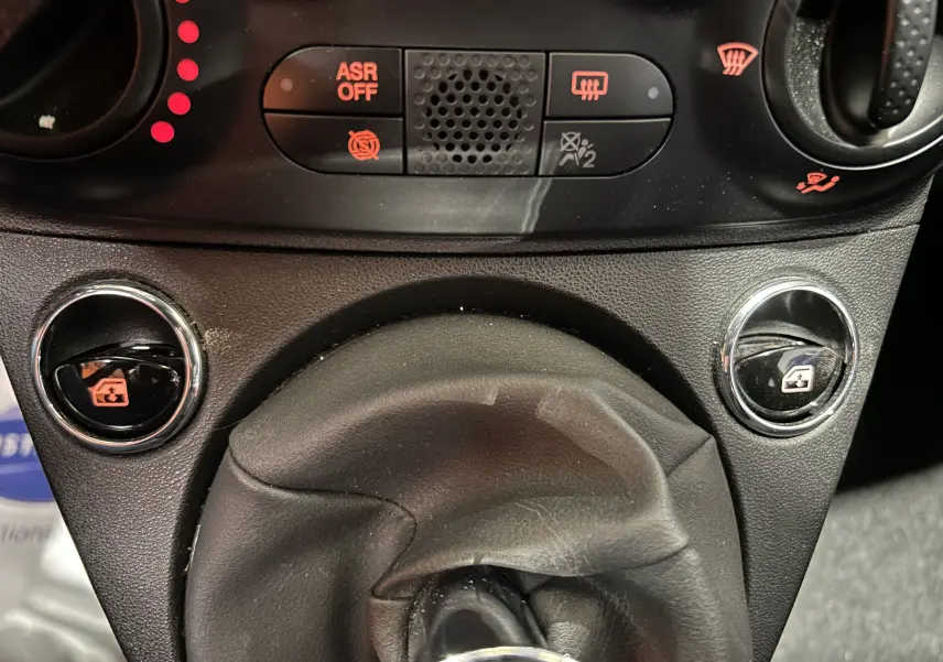 Gros plan sur la console centrale de la Fiat 500 2023, montrant le levier de vitesses manuel et les commandes des vitres électriques.