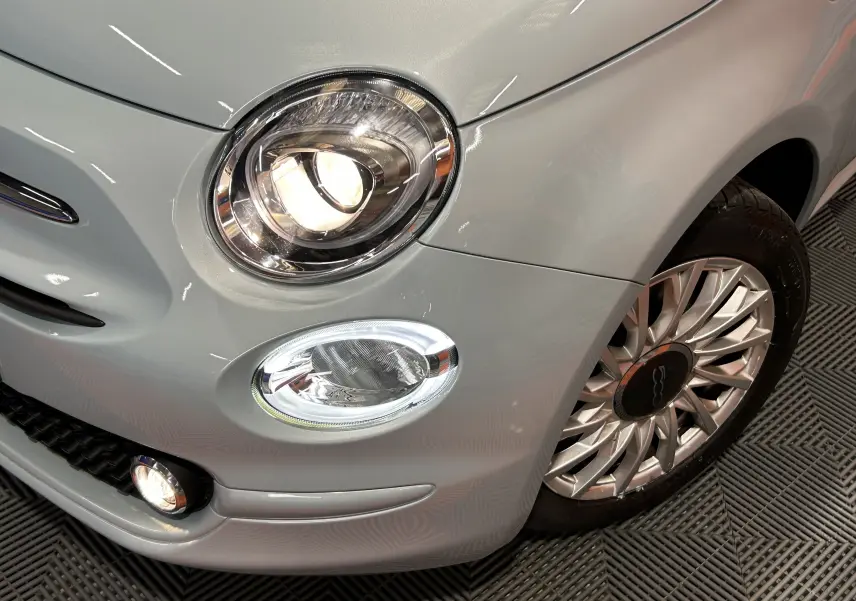 Gros plan sur l'avant droit de la FIAT 500 2023 en vert Rugiada, avec phare allumé et jante alu distinctive.