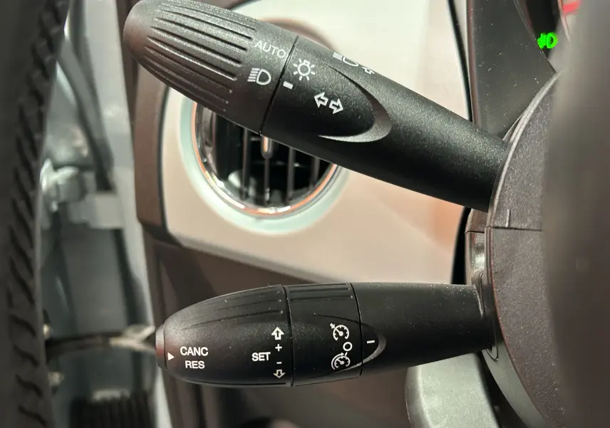 Gros plan sur les commandes de clignotants et régulateur de vitesse de la FIAT 500 2023, intérieur beige clair.