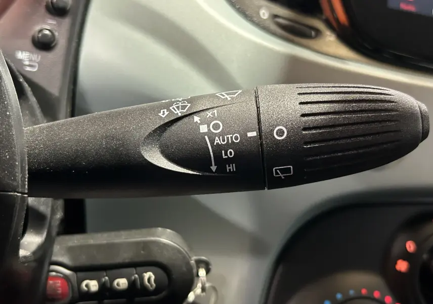 Gros plan sur la manette d’essuie-glace noire avec commandes blanches dans l’habitacle d’une FIAT 500 Rugiada Green 2023.