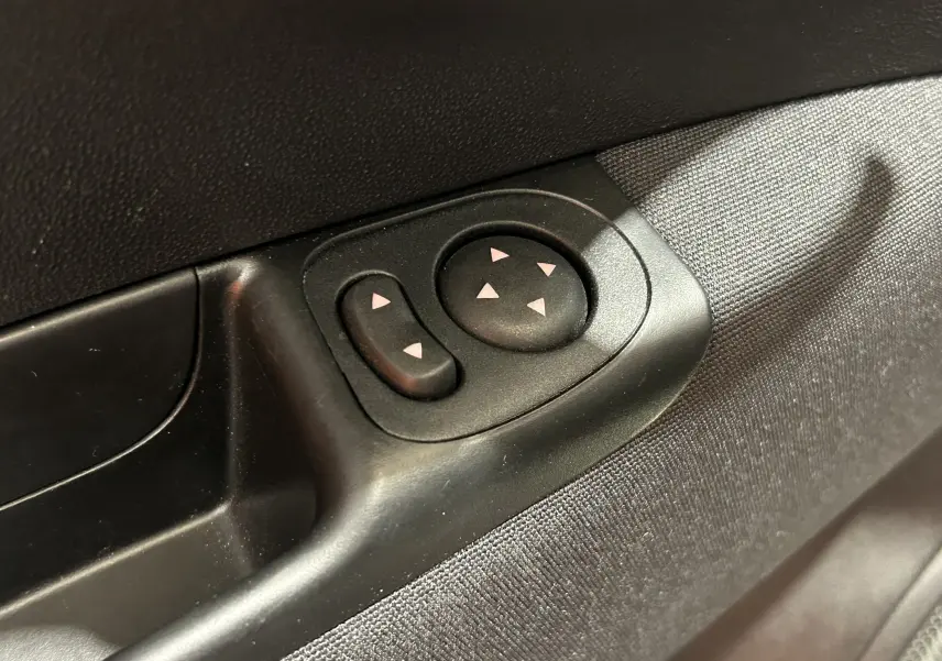 Gros plan sur les commandes de réglage des rétroviseurs côté conducteur de la FIAT 500 hybride 2023, intérieur noir et tissu gris.