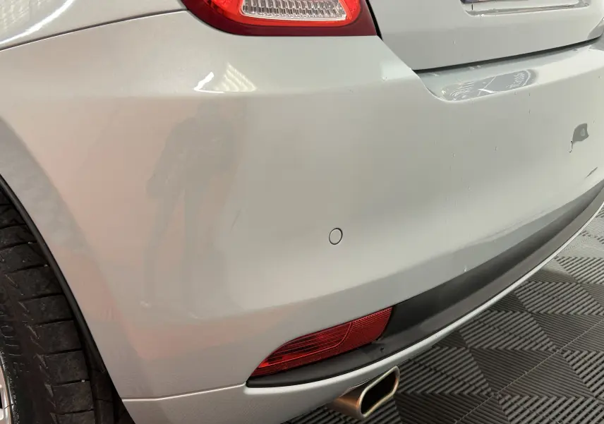 Gros plan sur le pare-chocs arrière droit gris clair de la FIAT 500 70 Hybride Pack Confort & Style avec feu et sortie d’échappement visible.