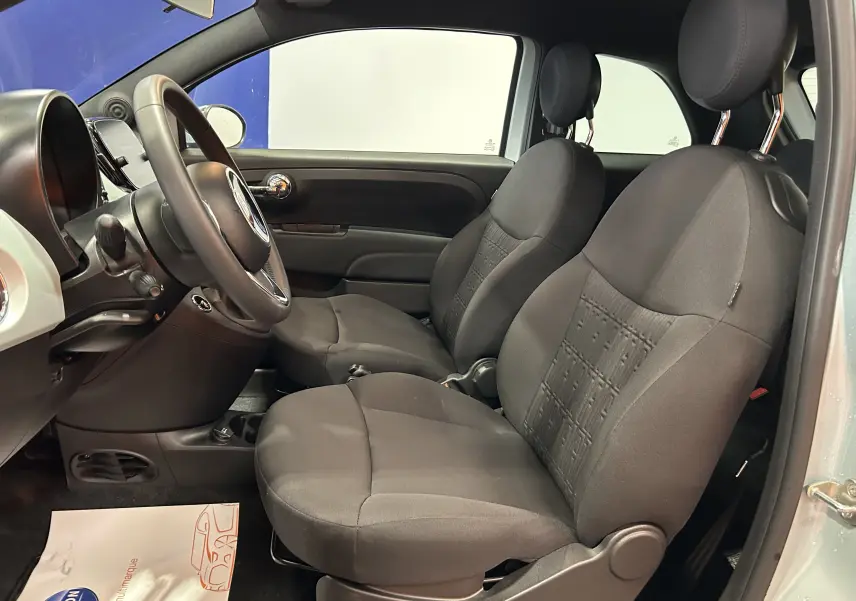 Vue intérieure côté conducteur de la Fiat 500 2023 Rugiada Green, sièges tissu noir et tableau de bord compact.