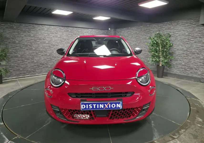 Vue avant d'une FIAT 600 rouge brillante avec logo 600 et plaque Distinxion en intérieur showroom.