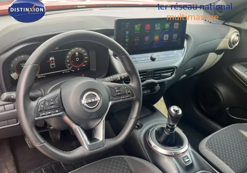 Vue intérieure du poste de conduite du Nissan Juke 2024, volant cuir et levier de vitesse manuelle visibles.