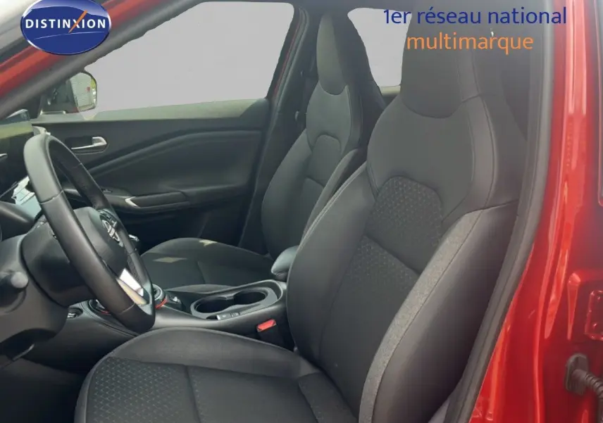 Vue intérieure côté conducteur du Nissan Juke rouge Fuji Metal 2024, sièges noirs en tissu et cuir avec volant multifonction.