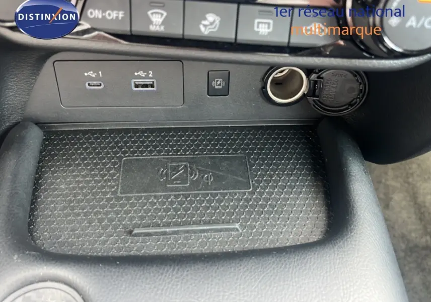 Détail de la console centrale du Nissan Juke 2024 rouge Fuji Metal, montrant les ports USB, prise 12V et zone de recharge sans fil.
