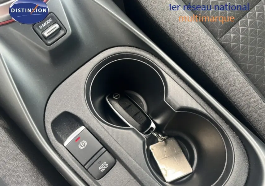 Vue rapprochée de la console centrale noire du Nissan Juke 2024 avec clé dans porte-gobelet et bouton frein à main électrique.