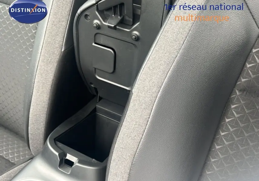 Gros plan sur la console centrale ouverte entre les sièges avant en tissu gris et simili cuir noir du Nissan Juke 2024.