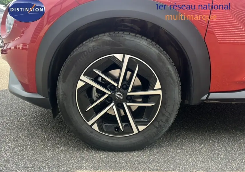 Gros plan sur la roue avant droite du Nissan Juke rouge Fuji Metal 2024 avec jante alliage noire et argent.