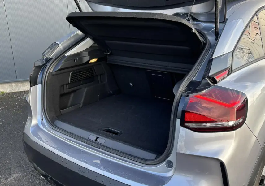 Coffre ouvert vu de l'arrière droit d'une Citroën C4 2024 gris Artense avec feux arrière LED et hayon relevé.