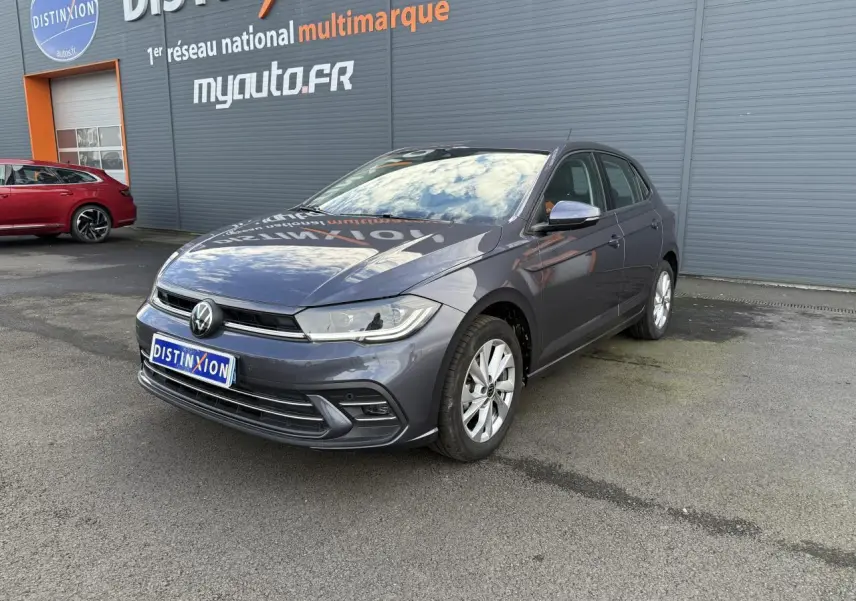 Volkswagen Polo gris cendre vue 3/4 avant droit, stationnée devant un mur gris avec logo Distinxion.