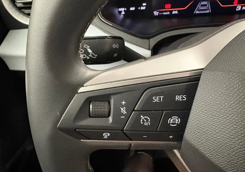 Gros plan sur les commandes au volant à gauche du SEAT Arona 2025, soulignant les fonctions régulateur adaptatif et assistance conduite.
