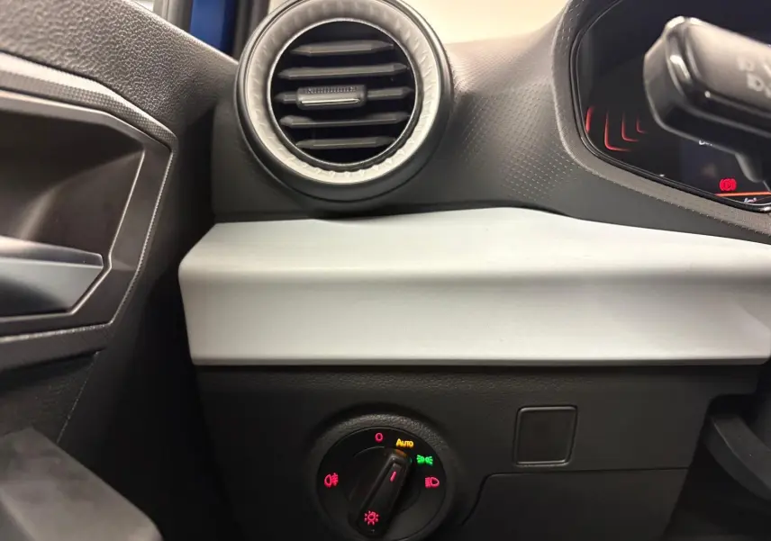 Détail intérieur côté gauche du tableau de bord du SEAT Arona 2025, avec commande des feux et aérateur rond.