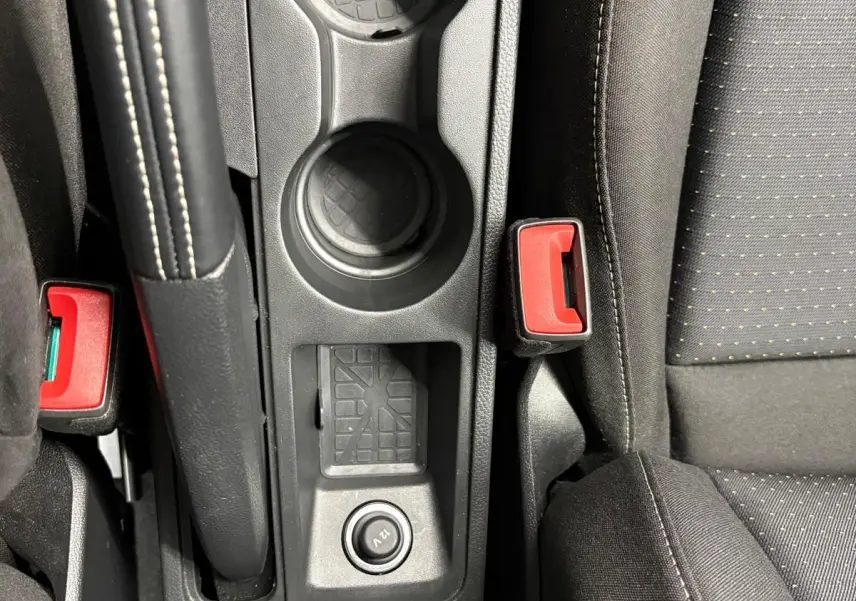 Gros plan sur la console centrale intérieure du SEAT Arona 2025, avec porte-gobelets, frein à main et bouton 12V.