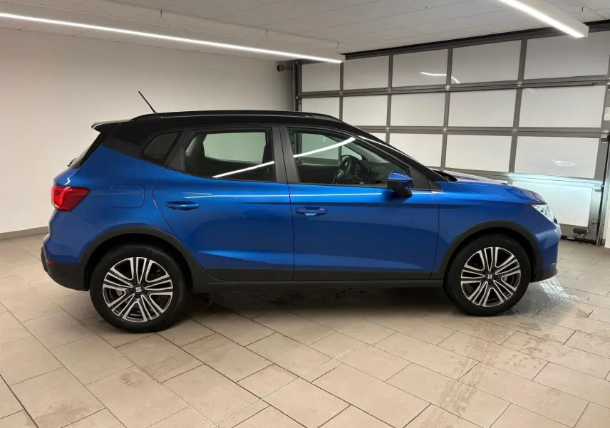 Vue de profil côté gauche d'un SEAT Arona 2025 bleu saphir avec toit noir, roues alliage et détails noirs contrastants.