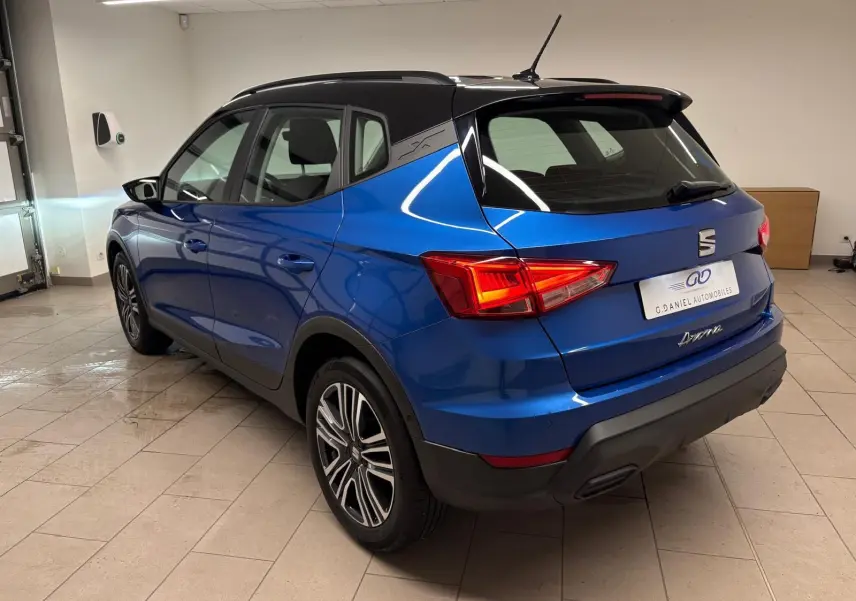 Vue 3/4 arrière droite d’un SEAT Arona 2025 bleu saphir avec toit noir, feux arrière allumés en intérieur.