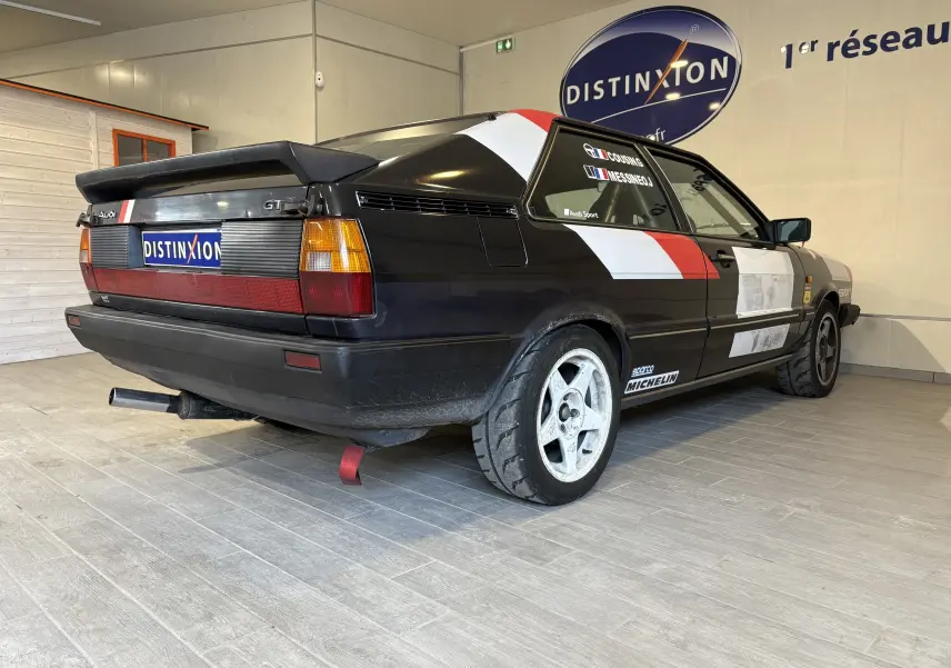 Audi Coupé GT noir vue 3/4 arrière droit avec bandes blanches et rouges, stickers de rallye et jantes sport.