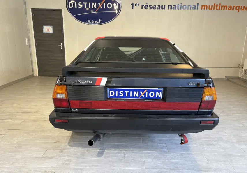 Vue arrière d'une Audi Coupé GT noire de 1983 avec aileron et bande rouge distinctive sur le coffre.