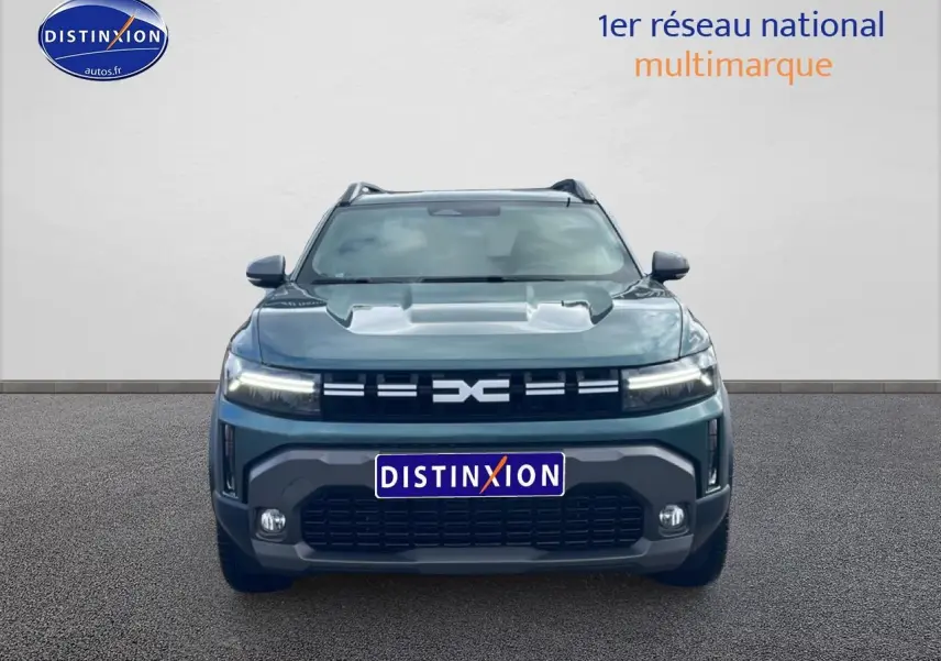 Vue avant du Dacia Duster 1.2 mild hybrid 140 Journey vert cèdre avec calandre distinctive et phares LED allumés.