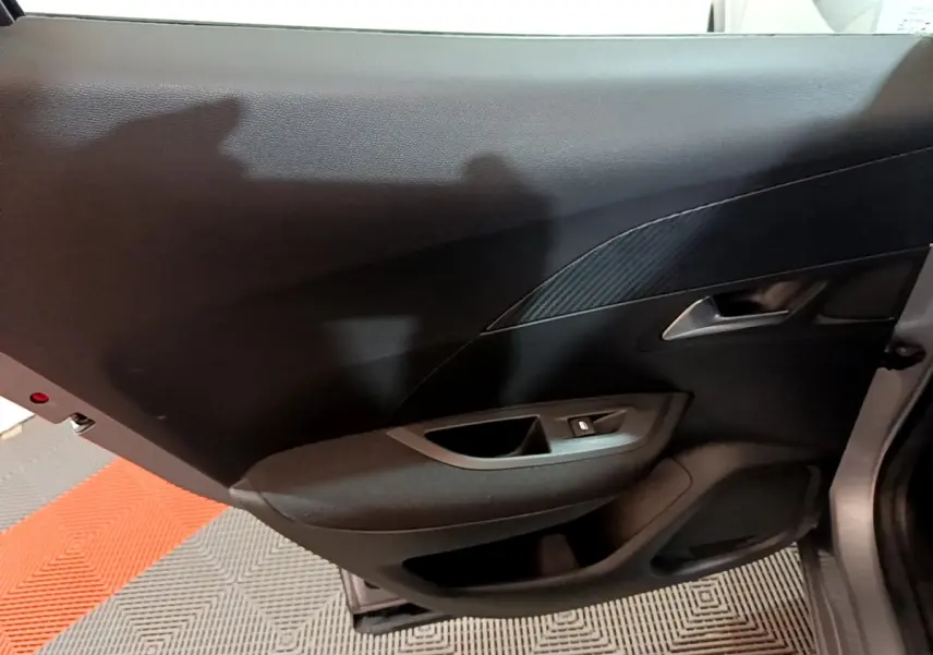 Vue intérieure du panneau de porte arrière gauche gris foncé du Peugeot 2008 avec poignée argentée et commande de vitre.