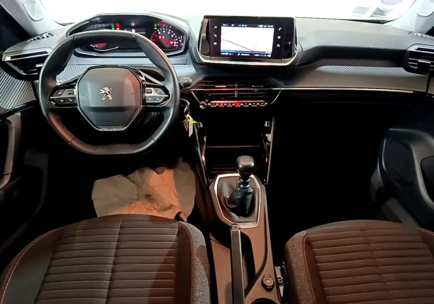 Vue intérieure avant du Peugeot 2008 gris clair 2021, volant cuir, écran tactile central et levier de vitesse manuel.