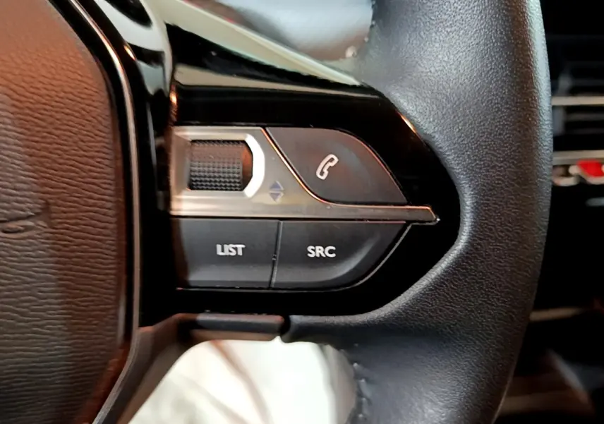 Gros plan sur les commandes gauche du volant cuir noir du Peugeot 2008 gris clair, avec boutons de téléphone et volume.