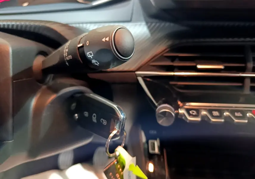 Gros plan intérieur sur la clé insérée et la commande d’essuie-glace du Peugeot 2008 gris clair, tableau de bord partiellement visible.