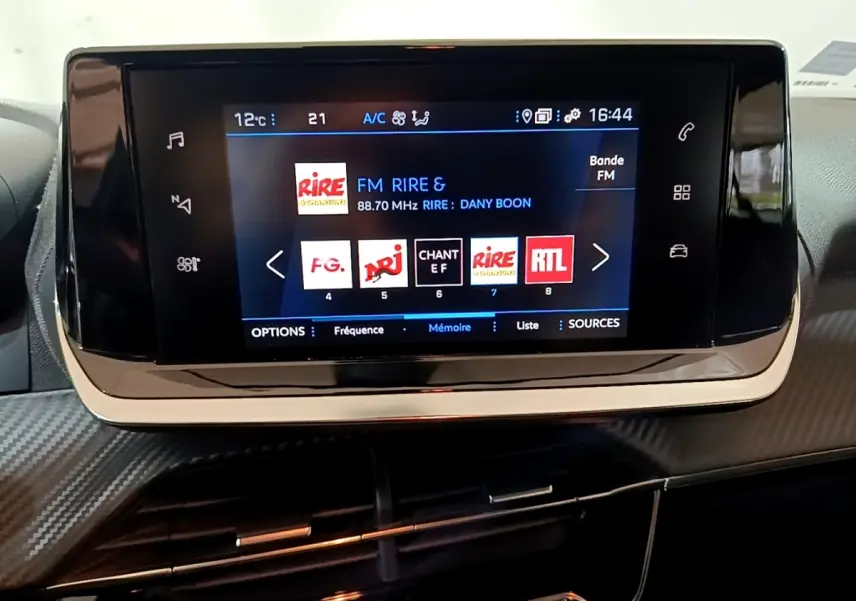 Écran tactile central du tableau de bord de la Peugeot 2008 gris clair, affichant les stations radio FM.