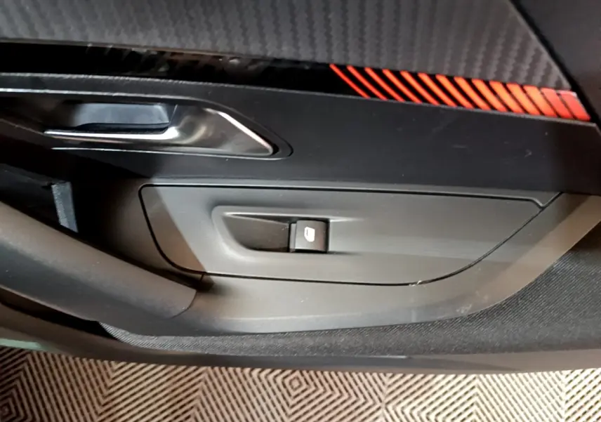 Gros plan sur la commande de lève-vitre côté conducteur avec insert décoratif noir et rouge dans une Peugeot 2008 gris clair.