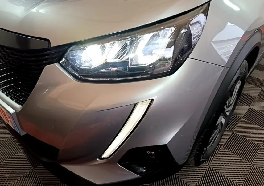 Gros plan sur l'avant droit gris clair du Peugeot 2008 2021 avec phares LED allumés et feux diurnes verticaux.