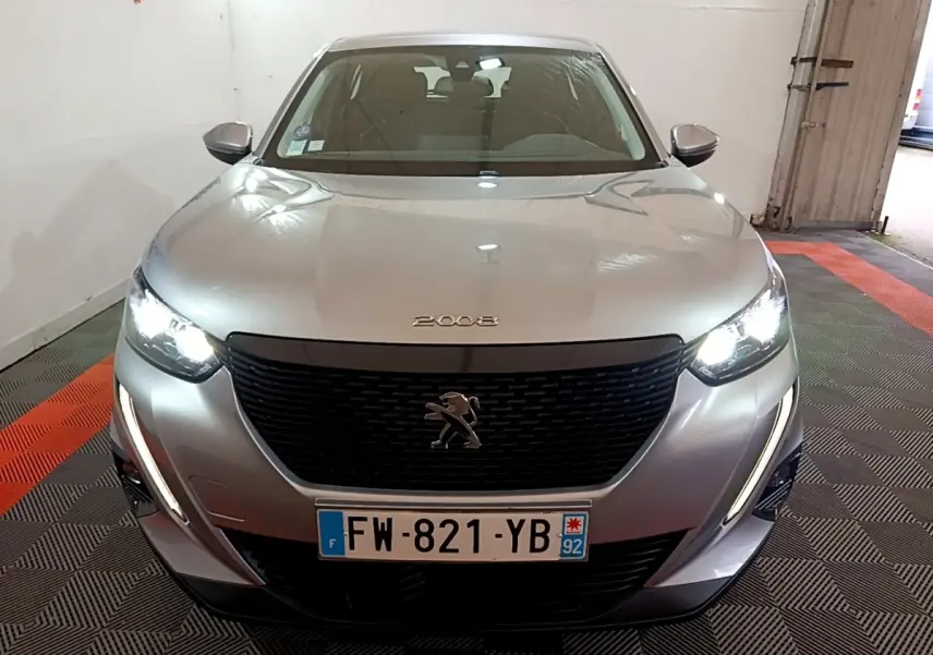 Vue frontale d’un Peugeot 2008 gris clair avec phares allumés et calandre noire distinctive.