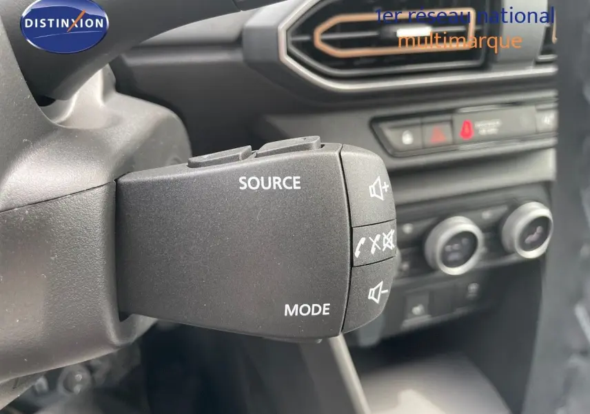 Gros plan sur la commande audio au volant de la Dacia Sandero Stepway 2024, intérieur noir avec commandes climatisation en arrière-plan.