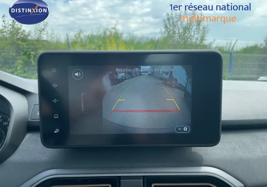 Écran central de la Dacia Sandero Stepway 2024 montrant la caméra de recul avec vue arrière sur un parking extérieur.