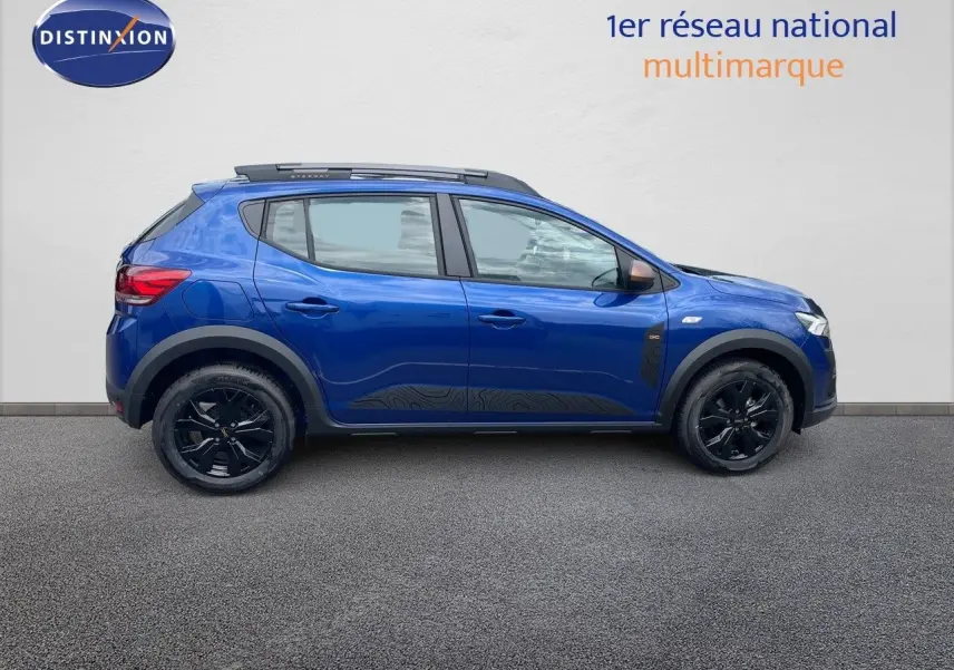Profil latéral droit d'une Dacia Sandero Stepway 2024 bleu Iron Metal avec jantes noires et barres de toit.